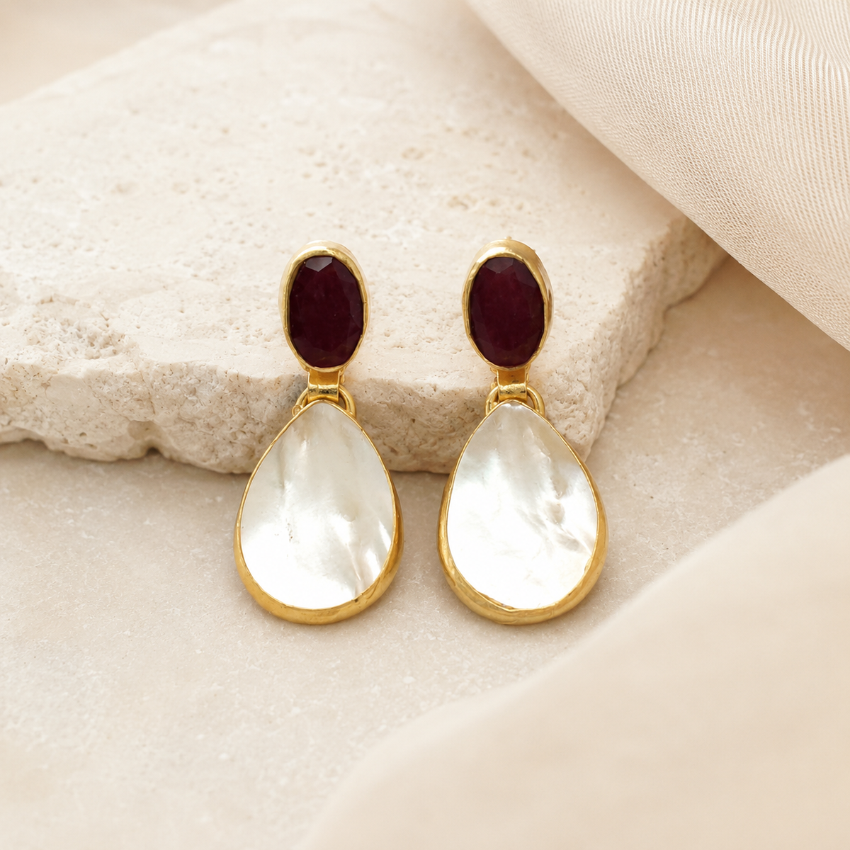 Pair of gold-plated drop earrings with red and pearl-like stones on a white background.