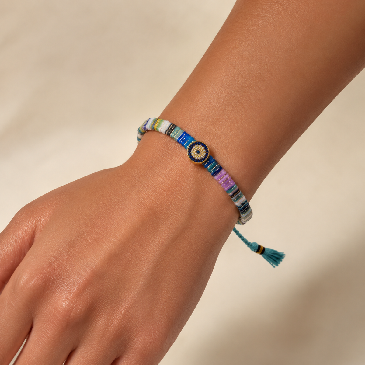 Multicolor woven fabric bracelet shown on a white background with a jeweled evil eye centerpiece.
