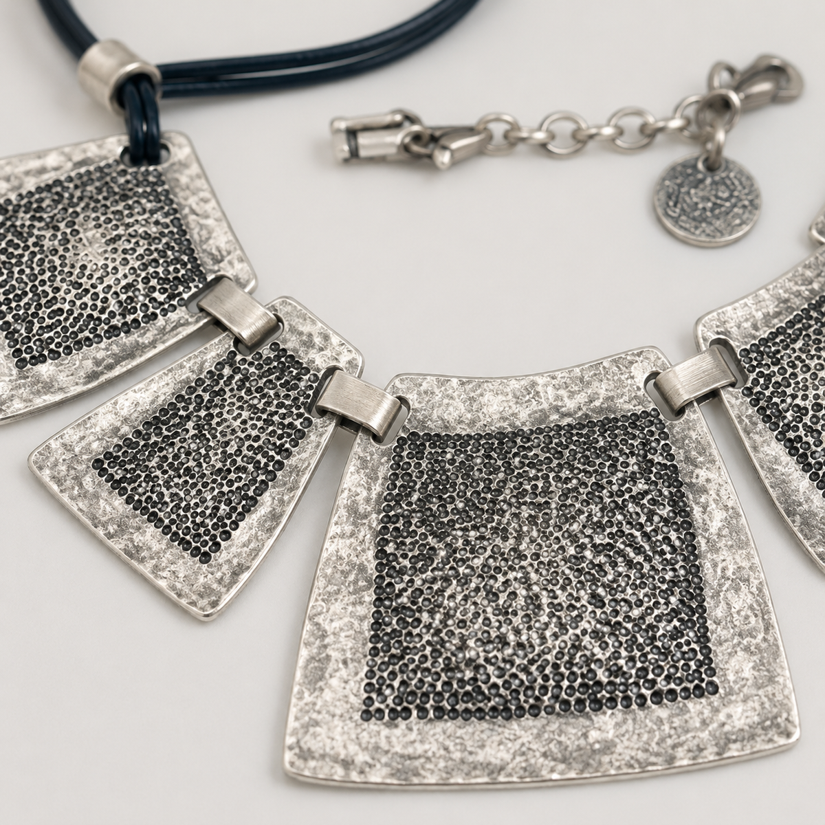 Close view of the necklace’s textured square plates and connecting links.