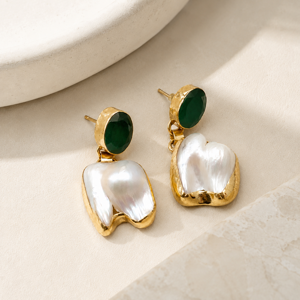 Angle view of gold-tone drop earrings with oval green stones and baroque pearls.