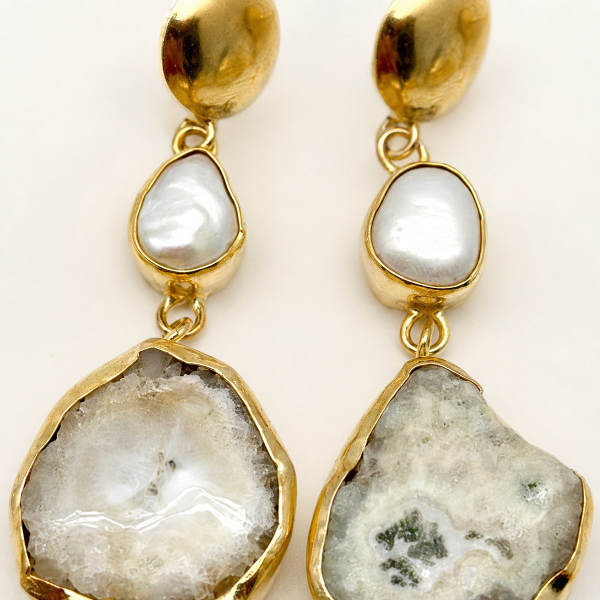 Close view of gold-plated earrings with white pearl-like centers and irregular stone-like drops.
