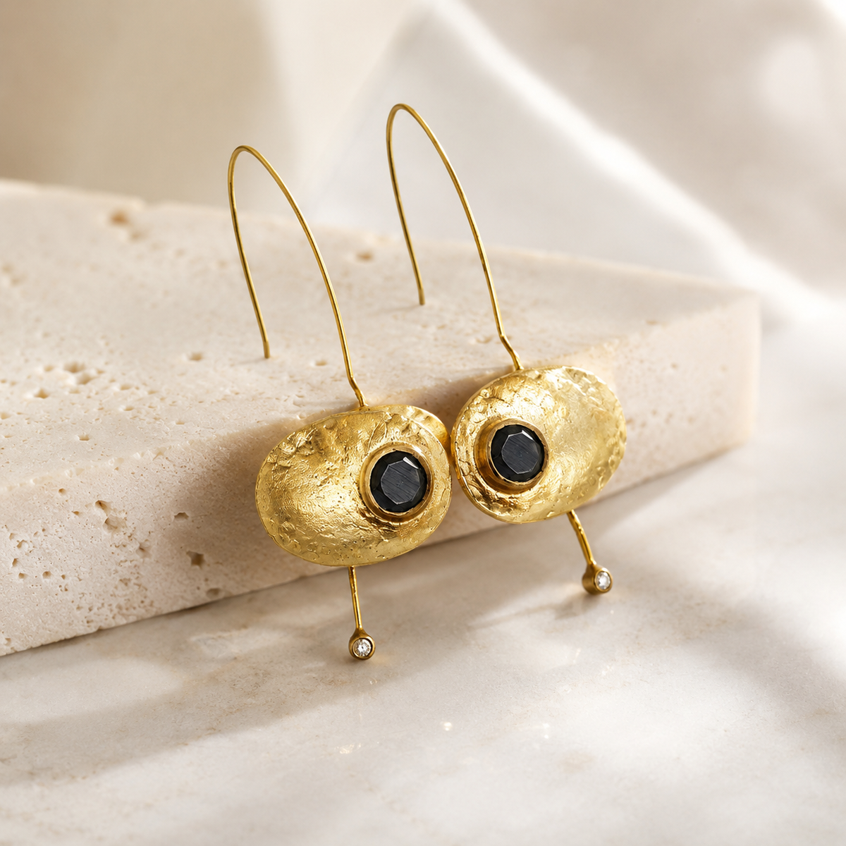 Angle view of oval black stone earrings with a gold-plated finish and slim drop.