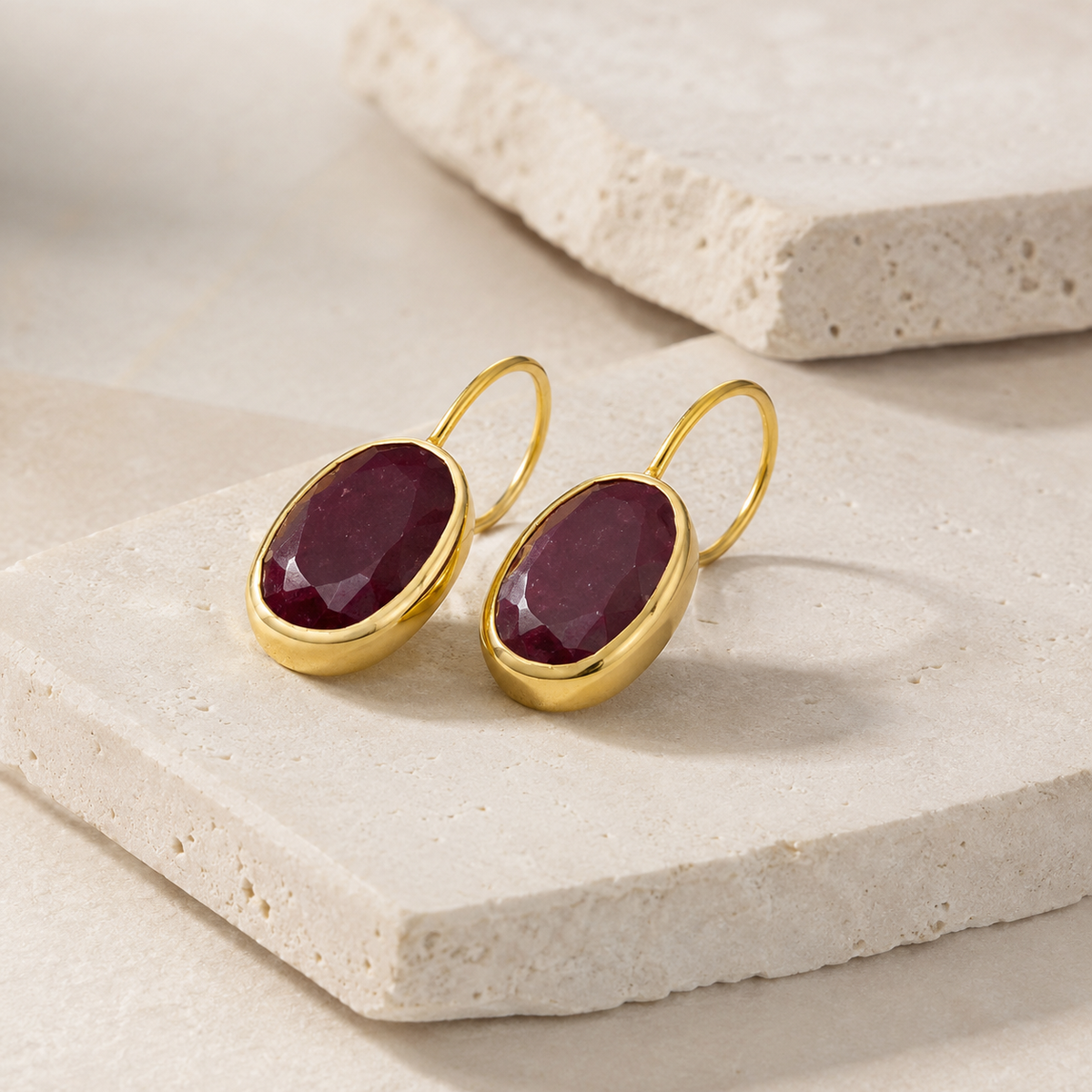 Side angle of gold-plated drop earrings with oval red stones.