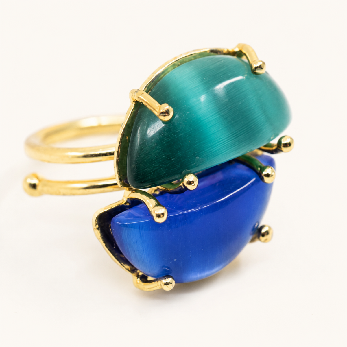 Close view of a gold-plated adjustable ring with two glossy blue and teal cat-eye style stones.