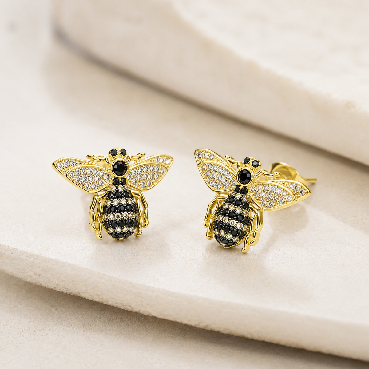 Angled view of bee stud earrings with black CZ accents and gold plating.