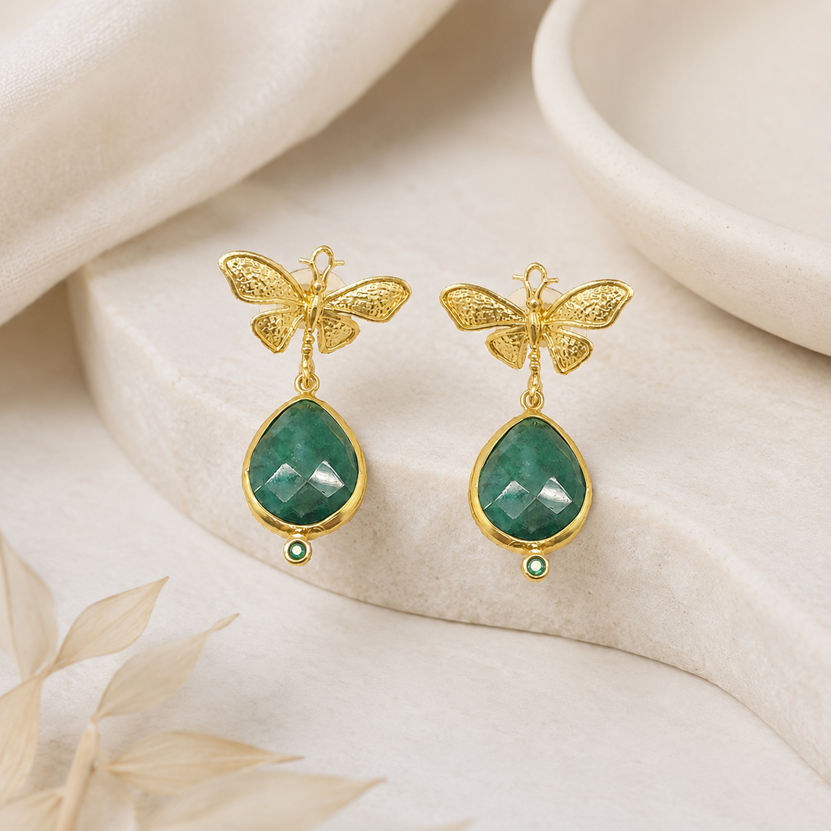 Gold butterfly statement earrings with faceted green teardrop stones.