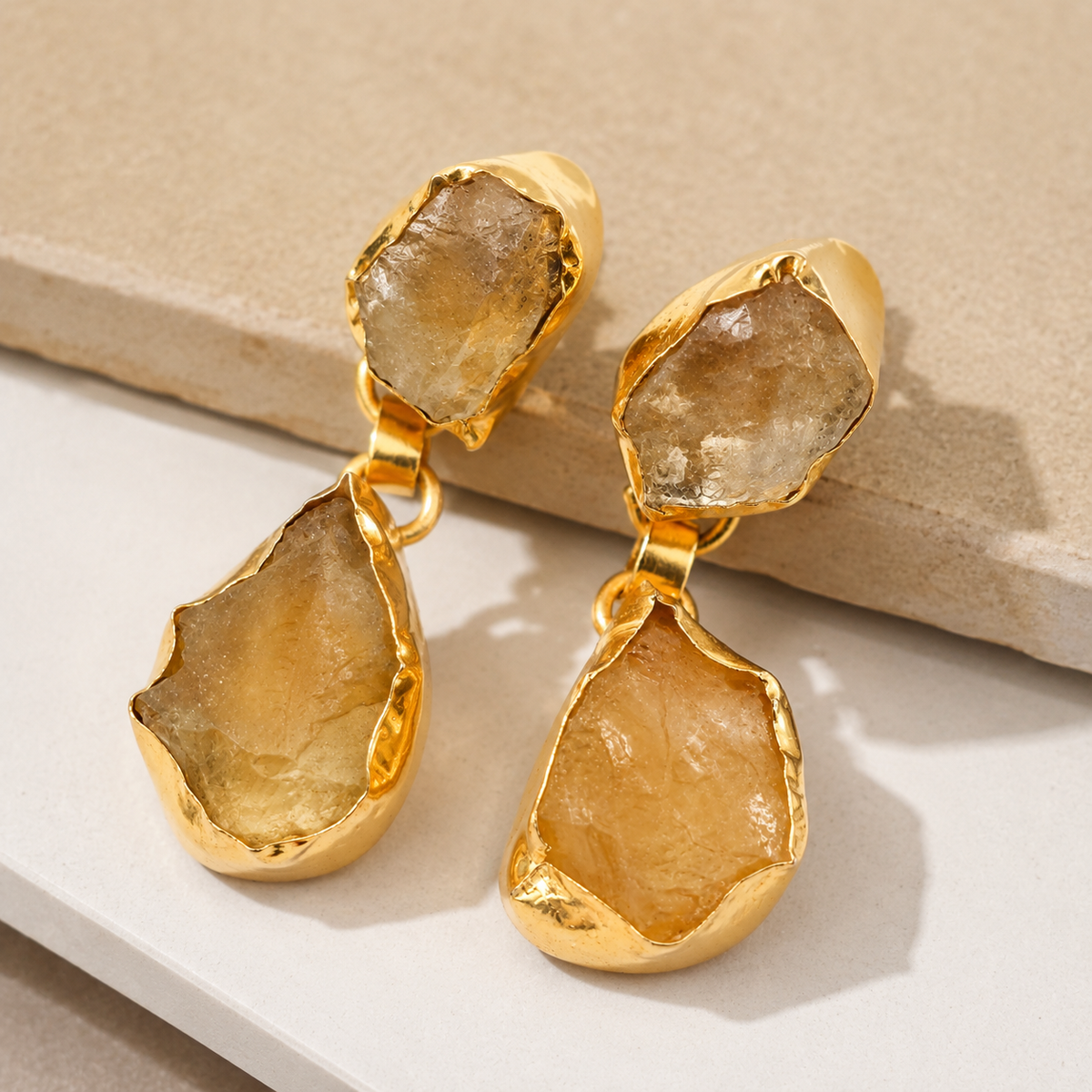 Angle view of gold-plated drop earrings with rough citrine-like stones.