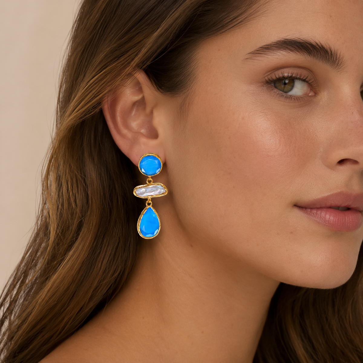 Gold-plated drop earrings with bright blue faceted stones and a pearl-like center.