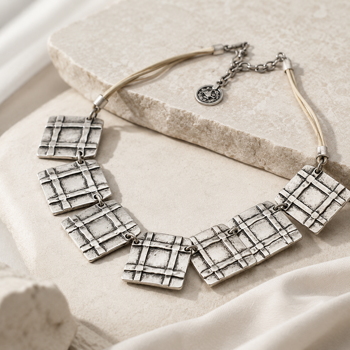Angled view of the beige cord grid square necklace with textured pendants.