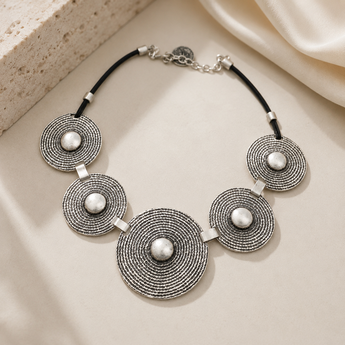 Silver-tone statement necklace with concentric disc pendants on a black cord.