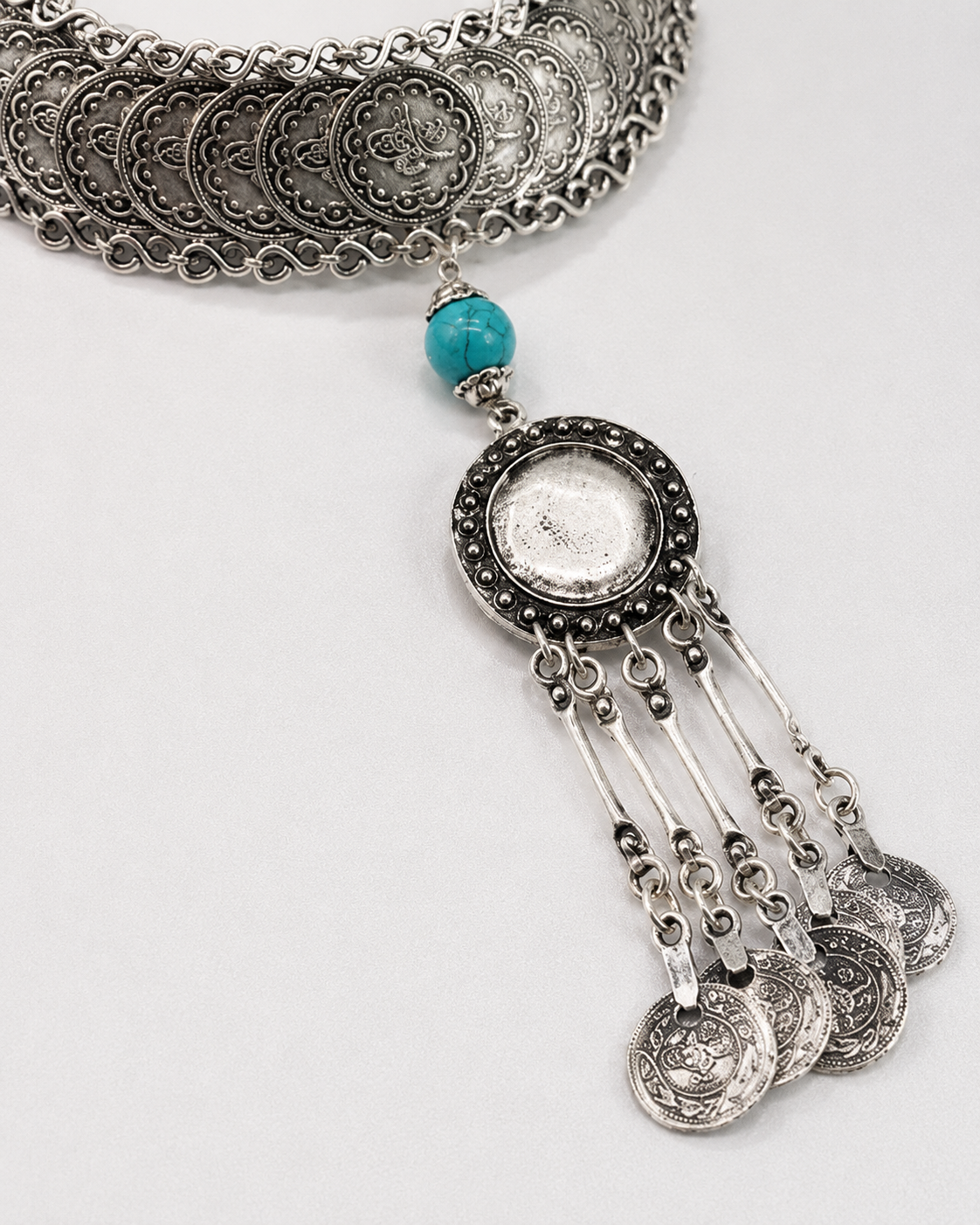 Close view of the silver-tone coin pendant and turquoise accent.