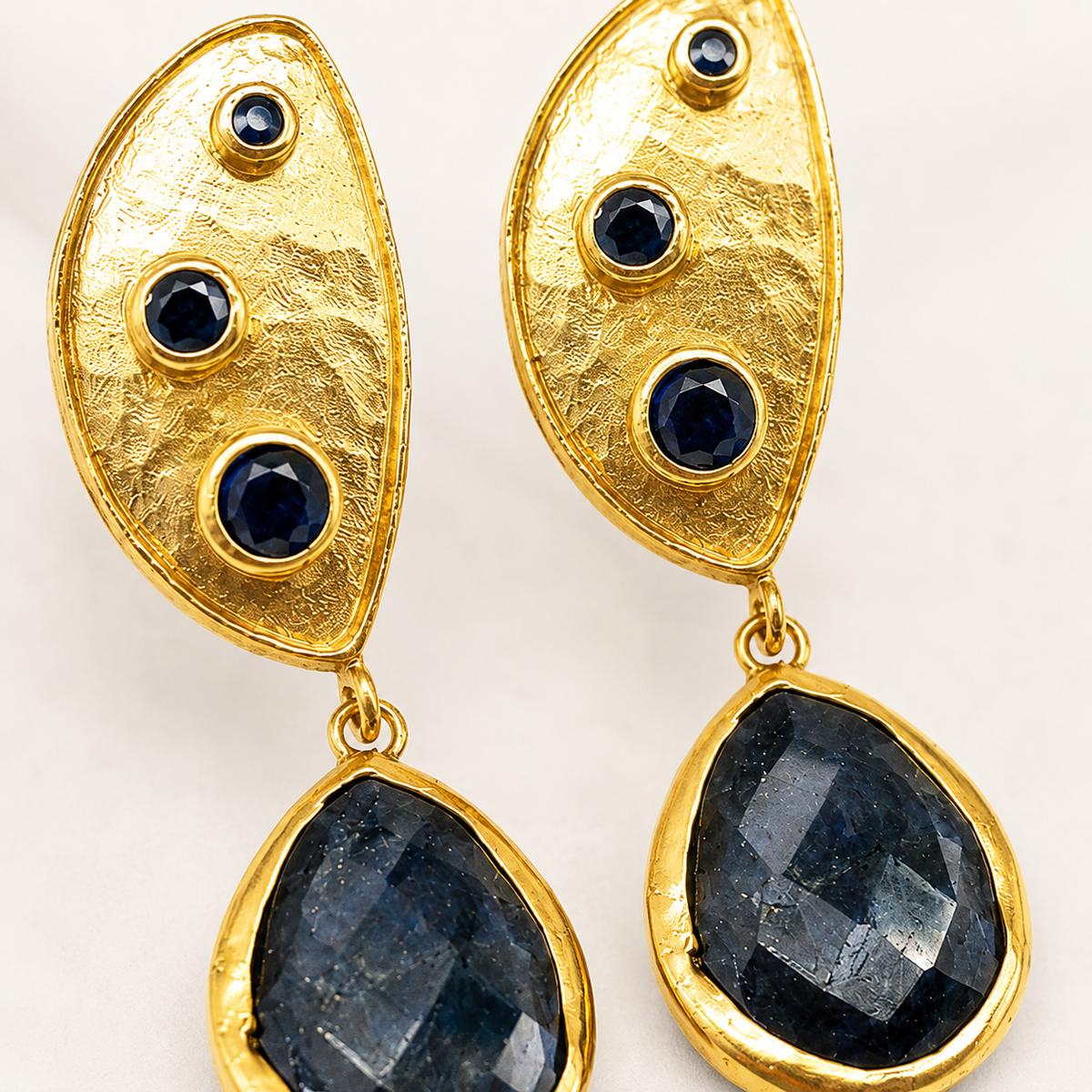 Close view of textured gold plated earrings with dark stones.