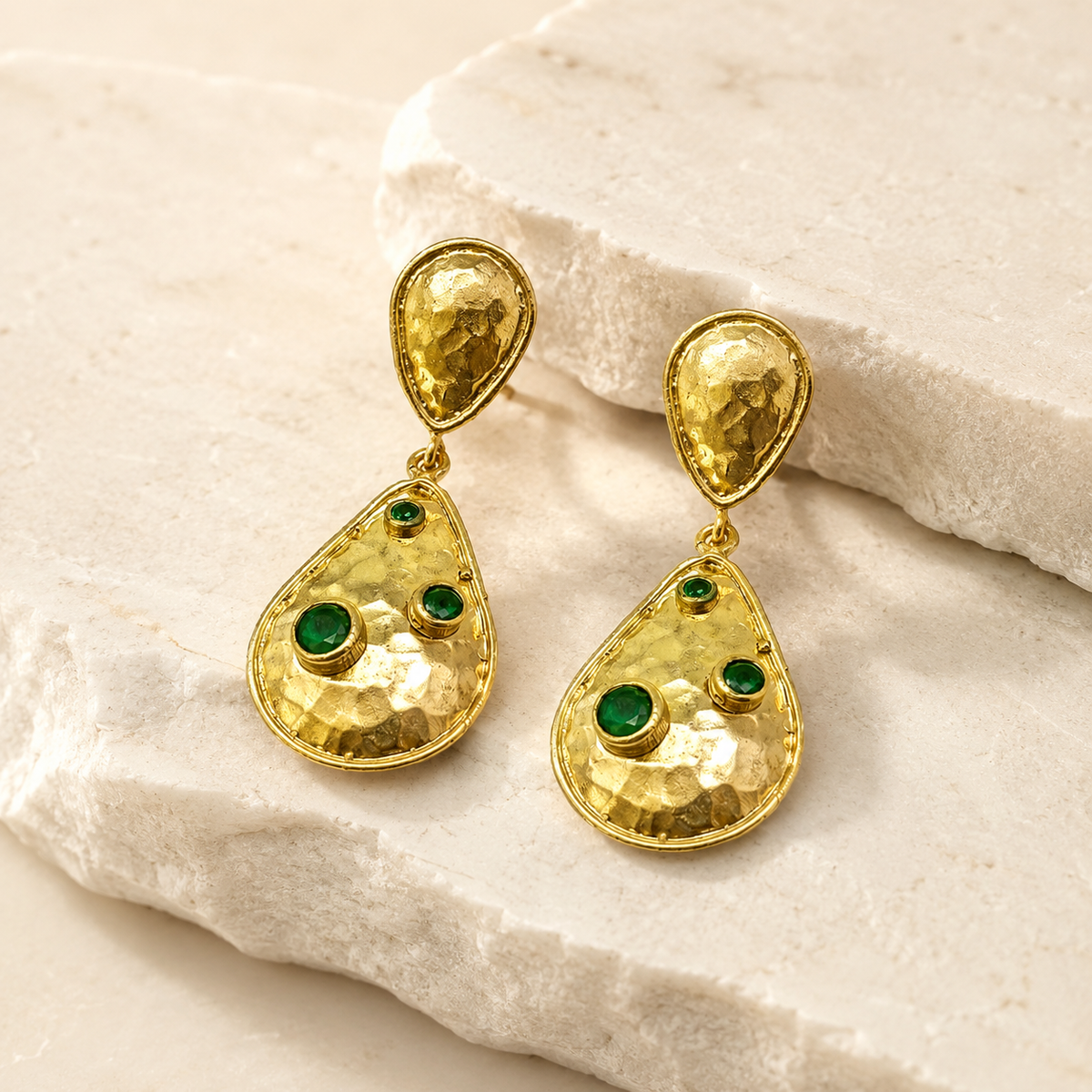 Angled view of double drop earrings in hammered gold-plated metal with green stones.