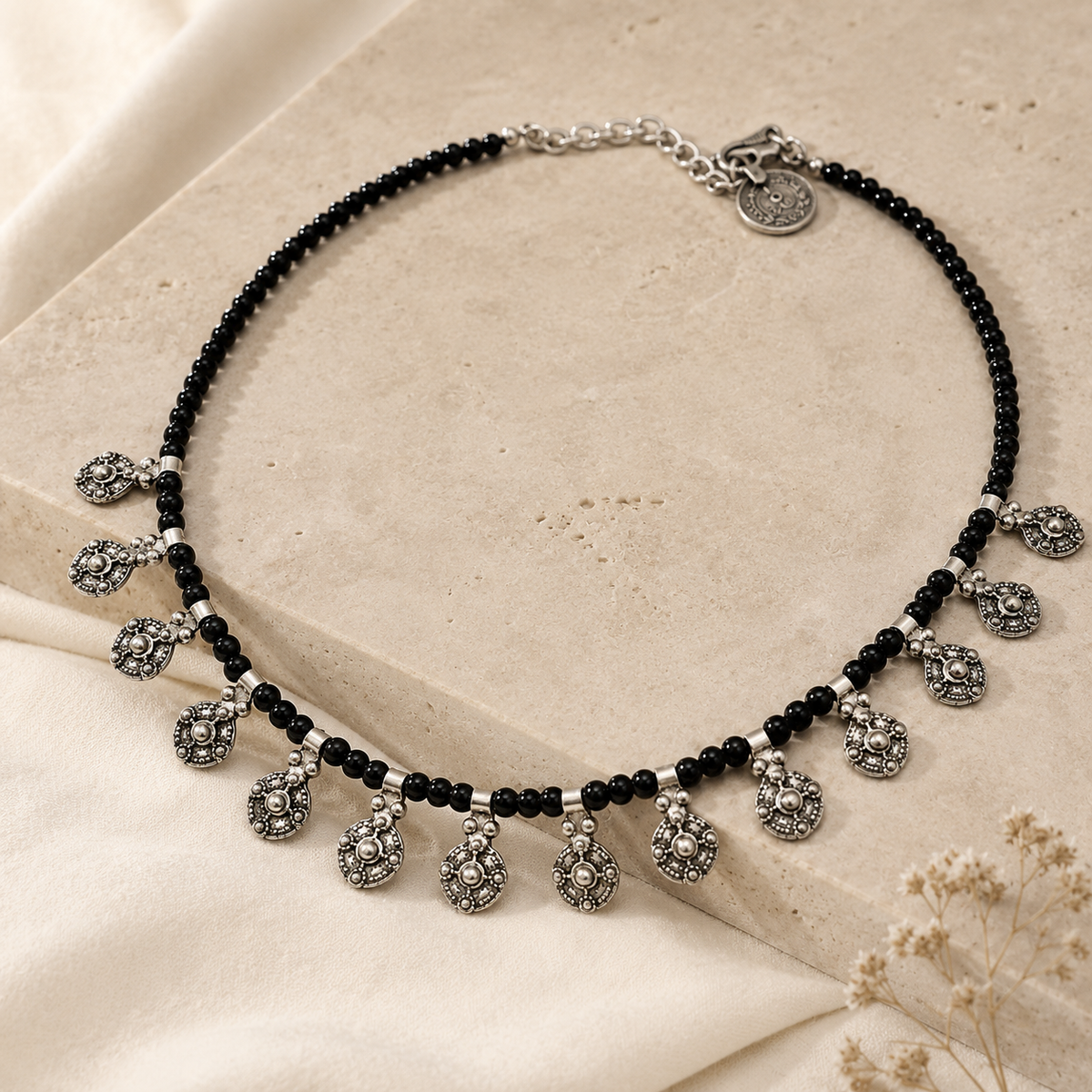 Angled view of a black bead filigree charm necklace with silver-tone details.
