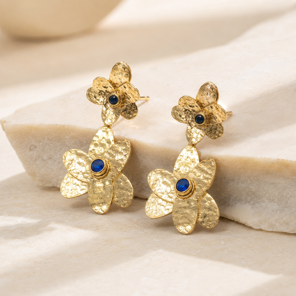 Angled view of double flower gold-plated earrings with blue stone centers.