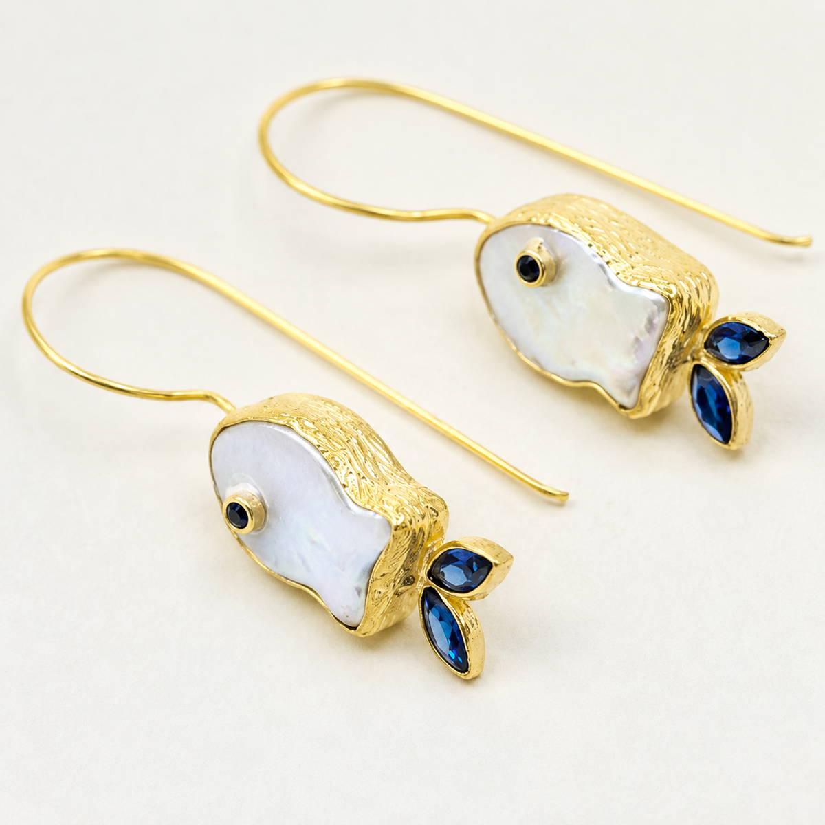 Close view of pearl-like fish earrings with gold-plated detail and blue accents.