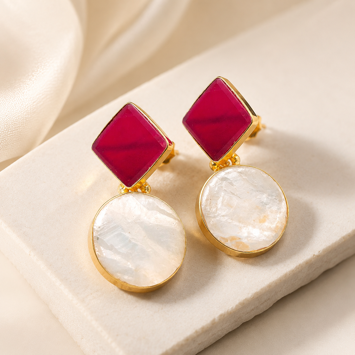 Angle view of gold-plated earrings with red geometric stones and round clear drops.
