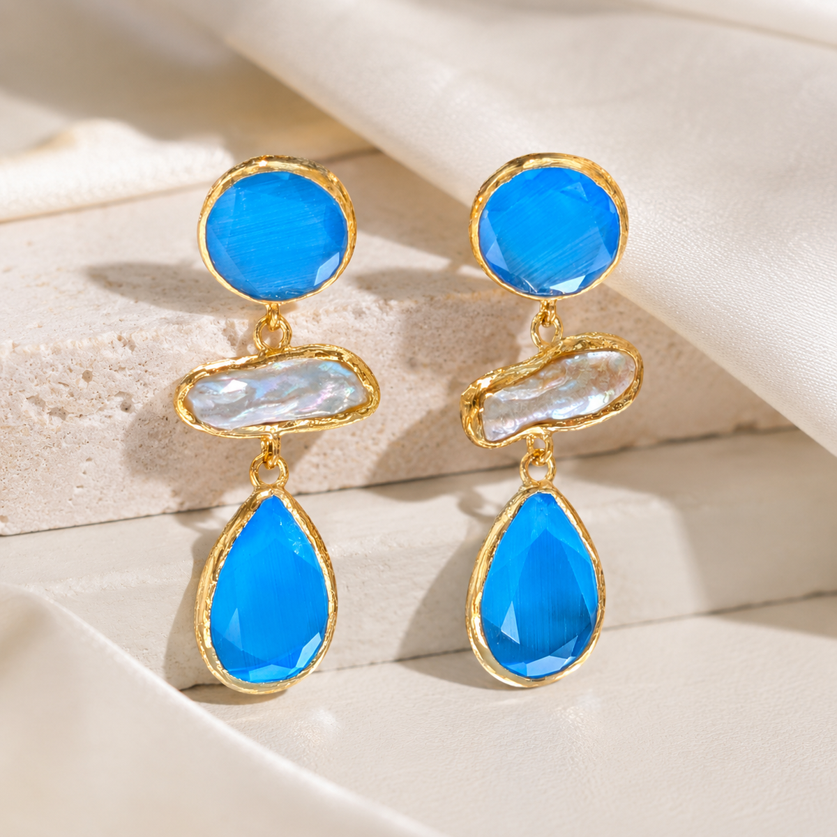Gold-plated drop earrings with blue stones and a pearl-like center on a white background.