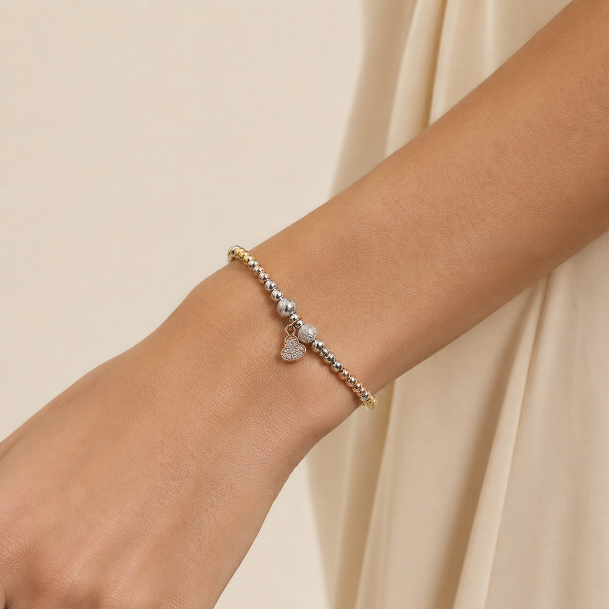 A heart bracelet with mixed-metal beads and a small charm shown on a white background.