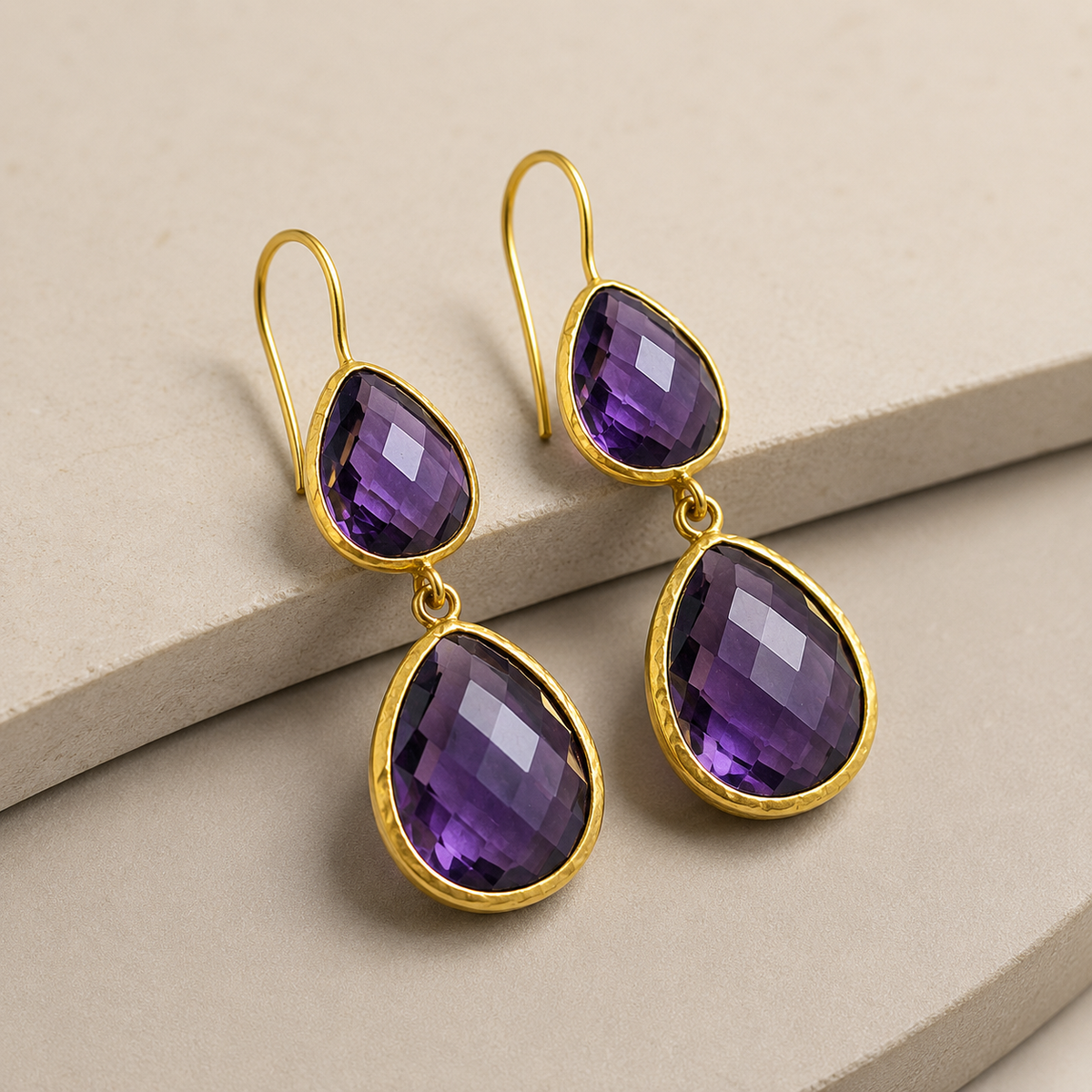 Angled view of gold-plated drop earrings with faceted amethyst stones.