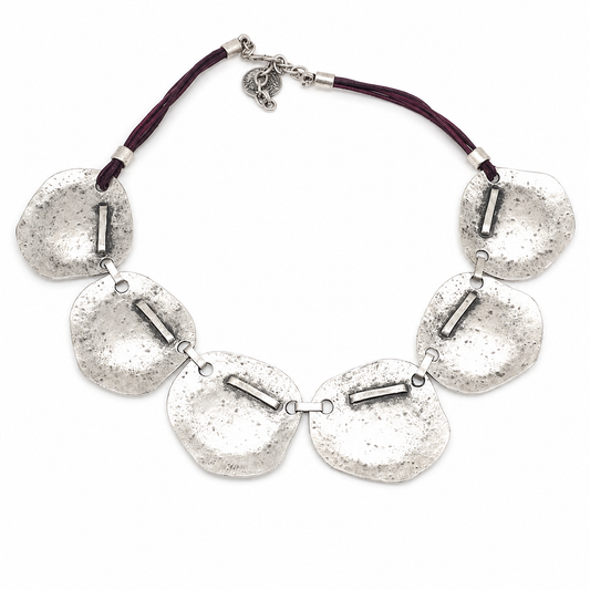 Hammered silver plate necklace with a sculptural linked design and dark cord detail.