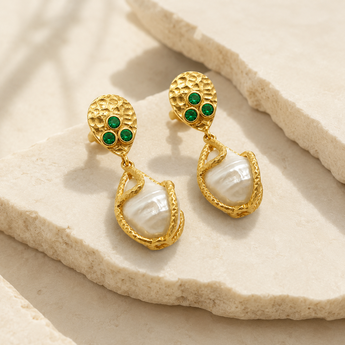 Angle view of gold-plated drop earrings with textured detailing, green CZ stones, and a pearl-like drop.