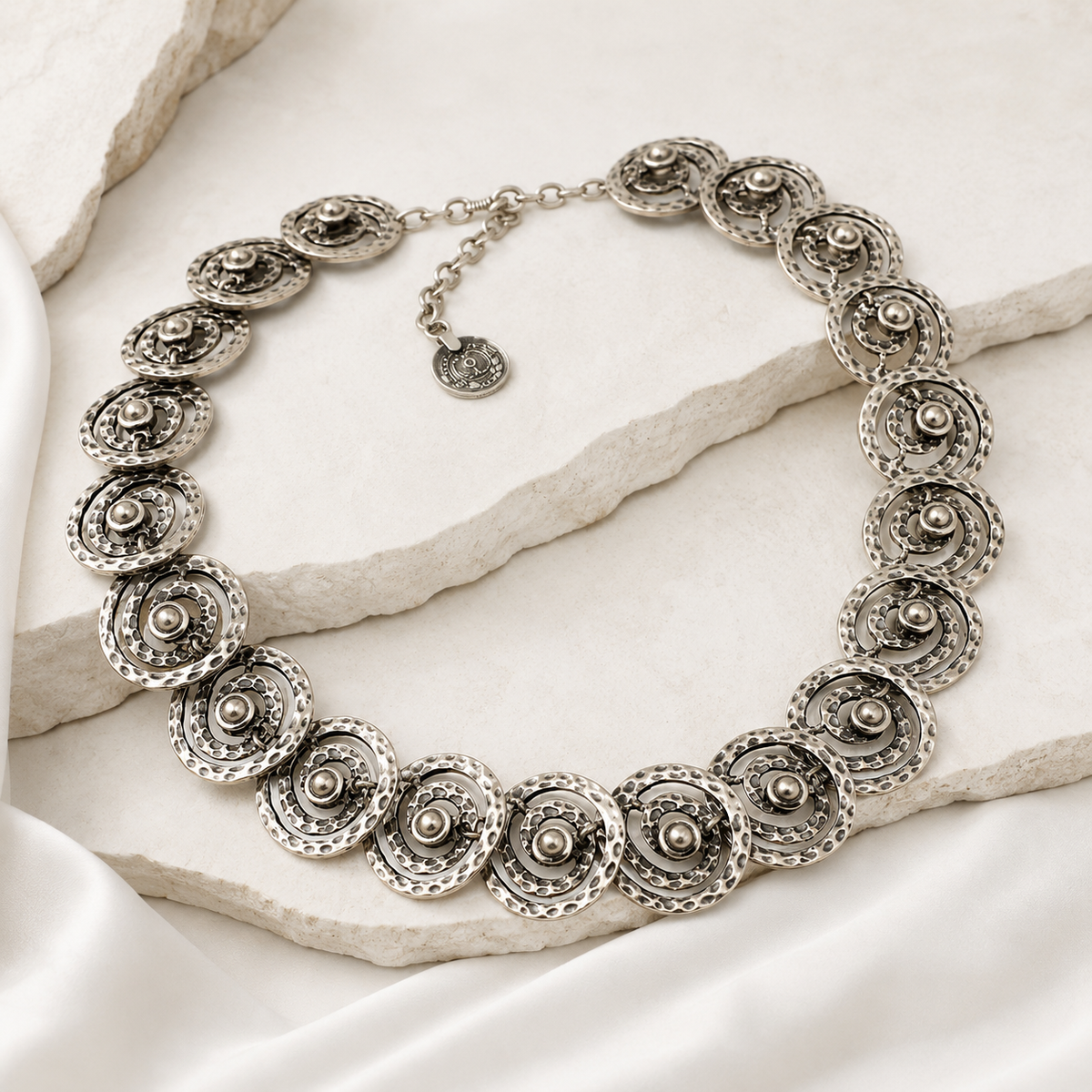 Silver-tone statement necklace with circular spiral links styled on a soft neutral surface.