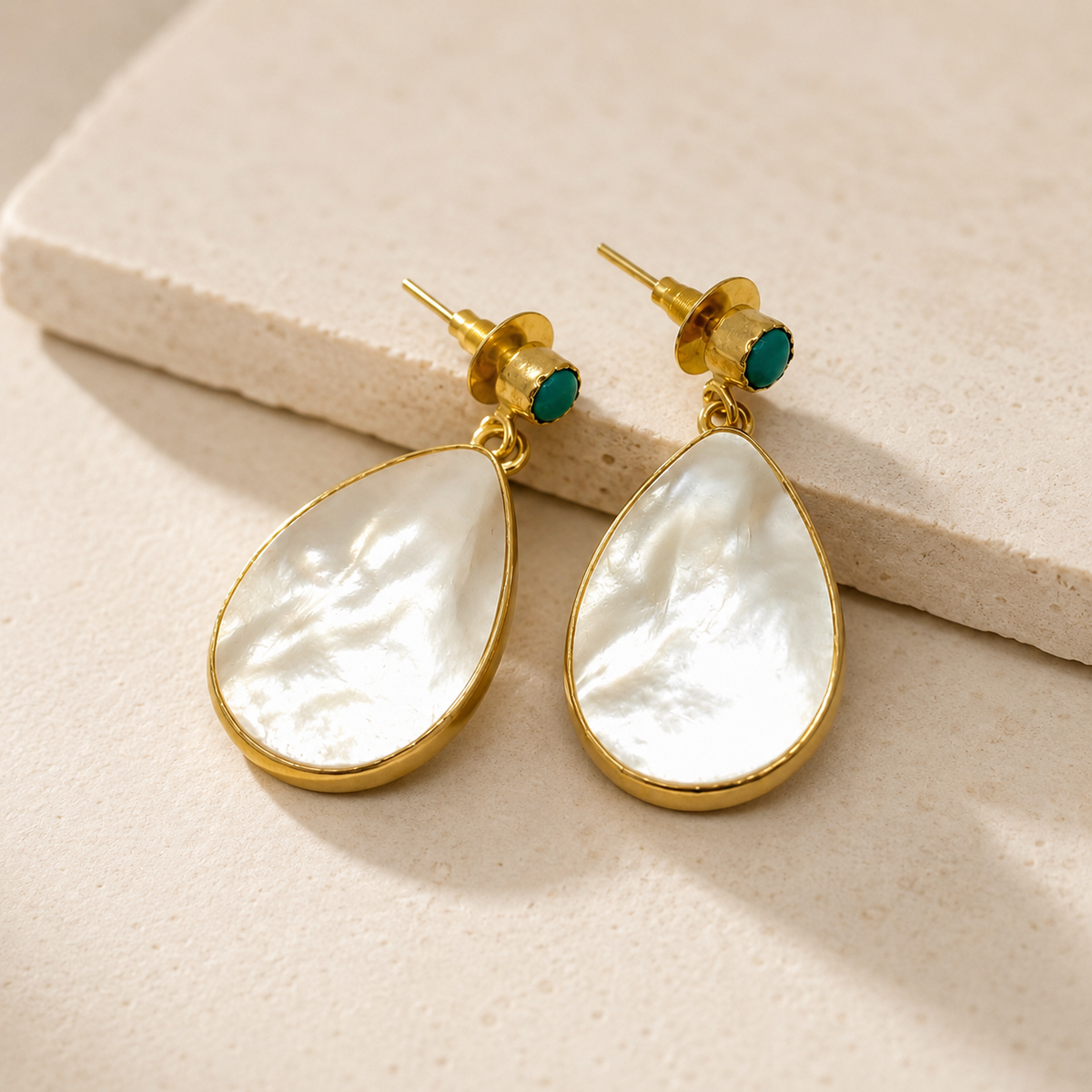 Angled view of drop earrings with mother of pearl, turquoise, and gold plating.