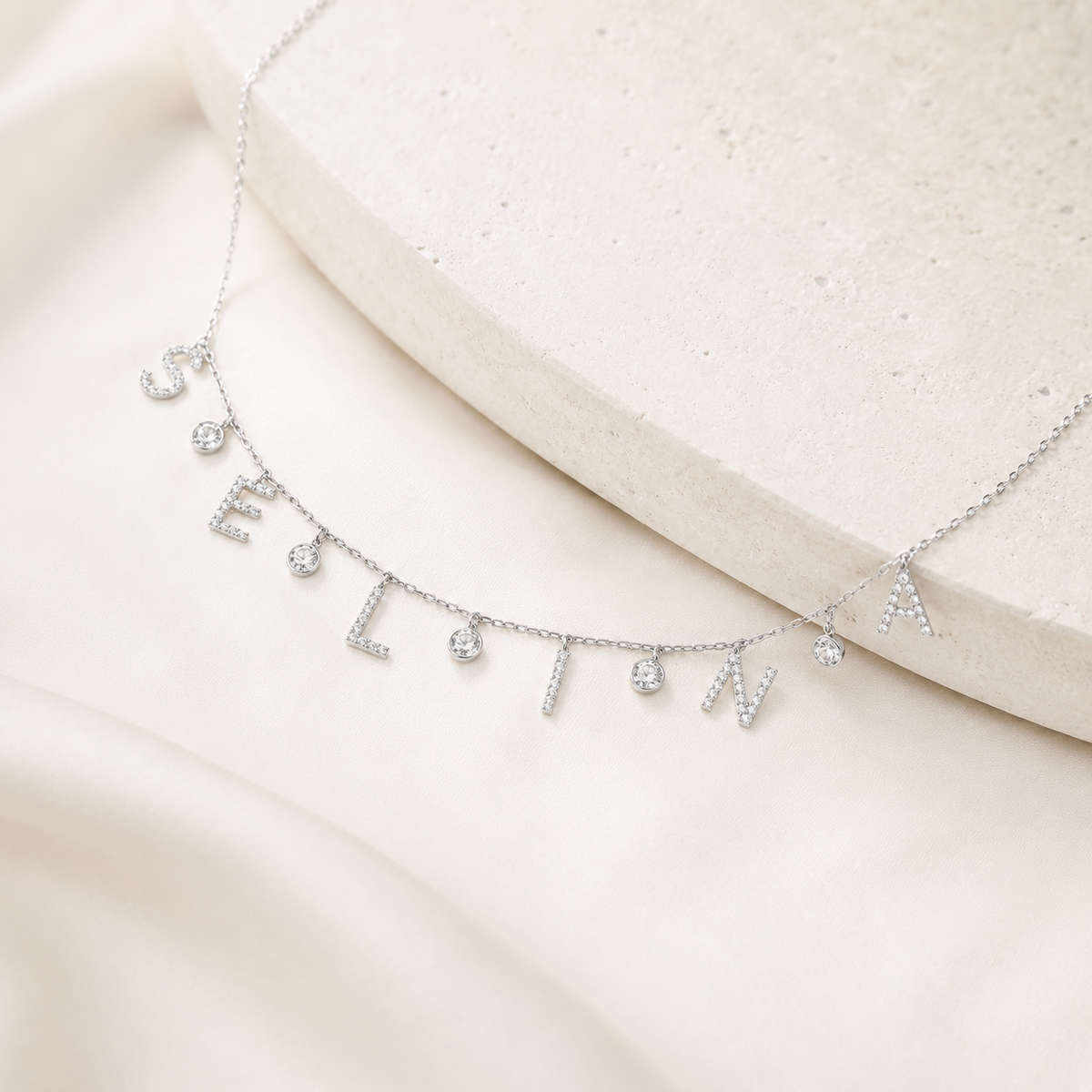 Angled view of a silver-tone name necklace with drop letters and a fine chain.