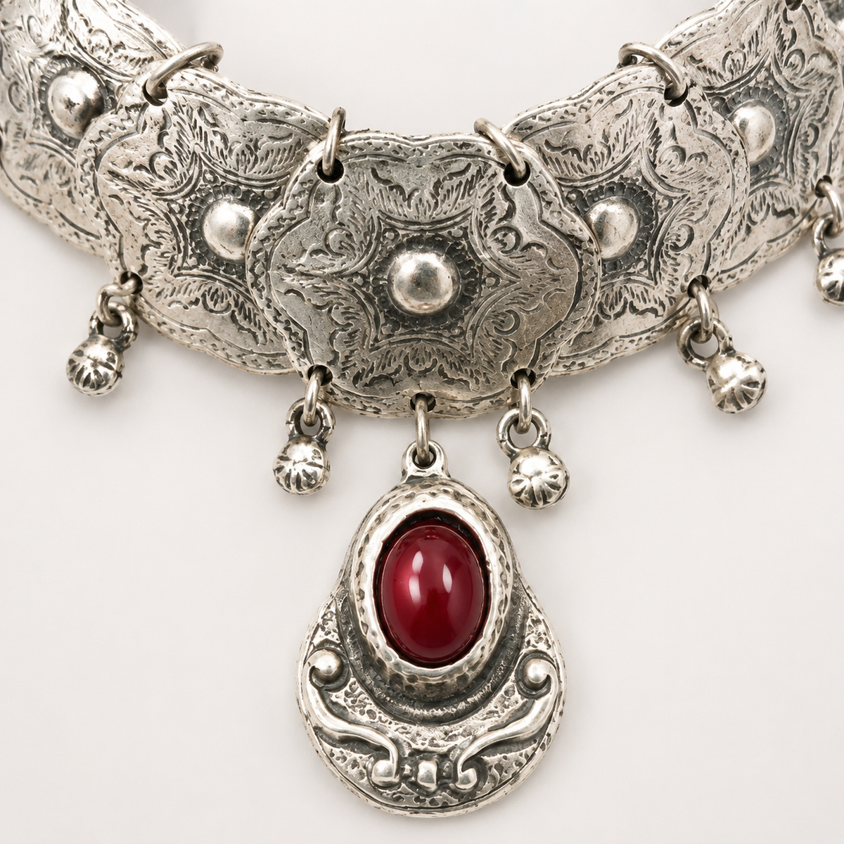 Close view of the engraved silver-tone plates and red stone pendant.