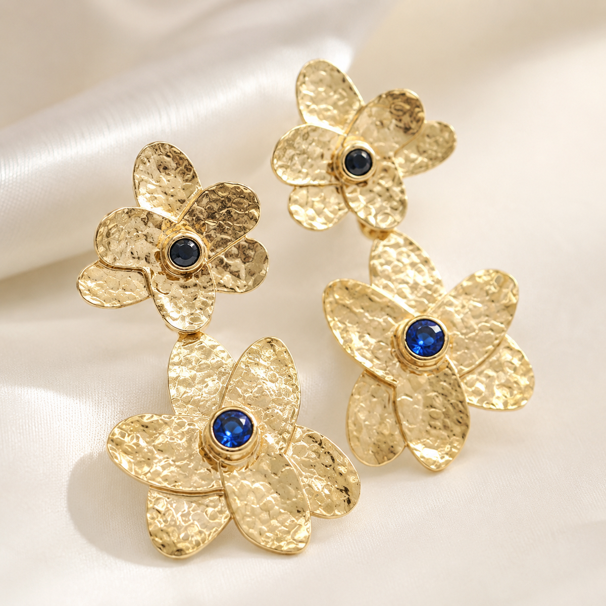 Close view of hammered gold-plated flower earrings with blue stone details.