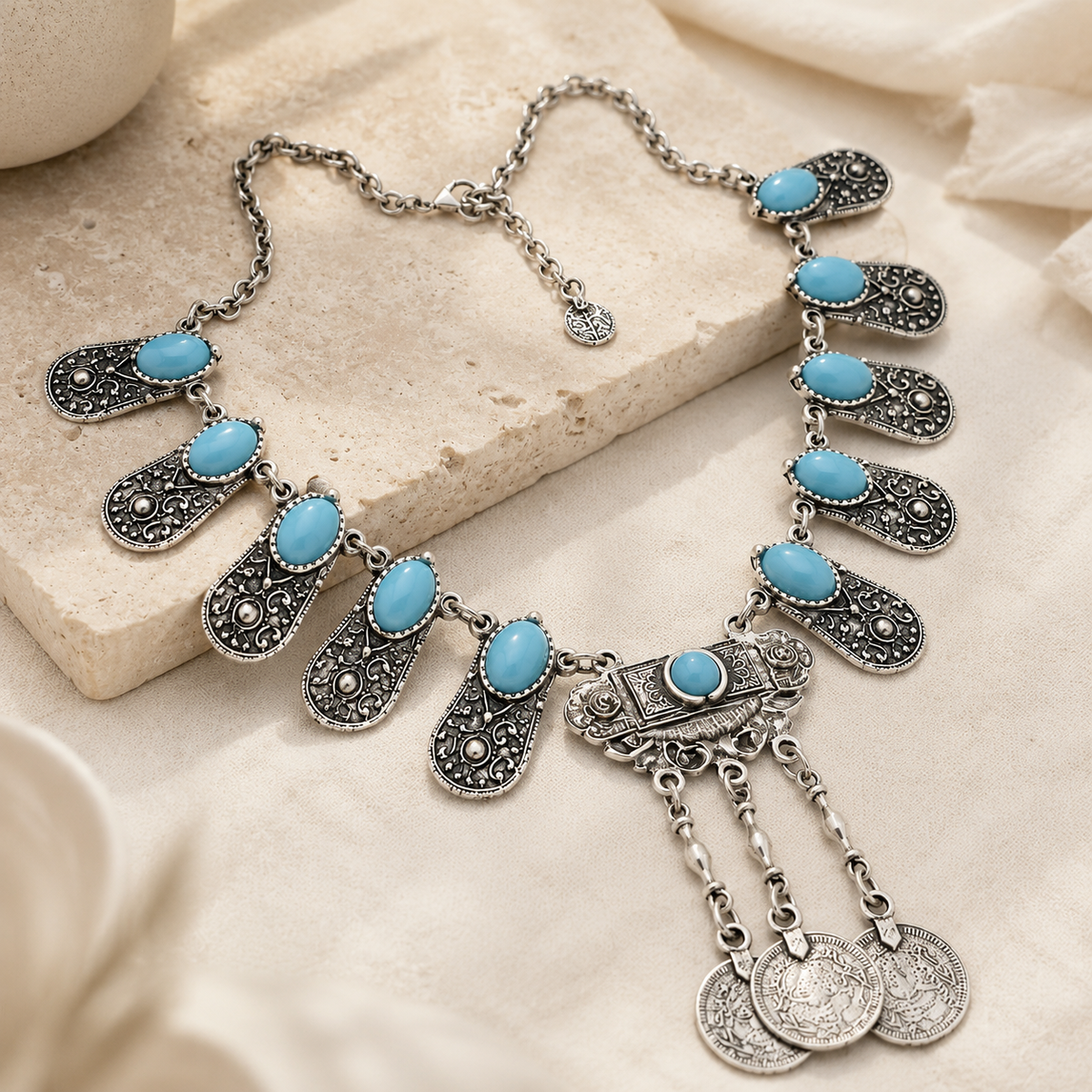 Angled view of a silver engraved panel pendant necklace with blue stones and dangling charms.