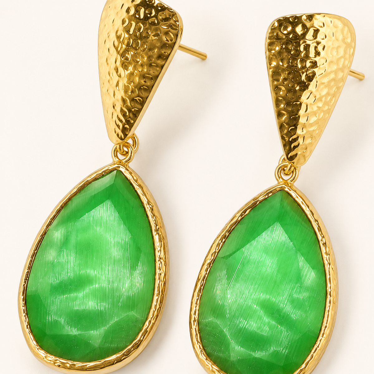 Close view of green teardrop earrings framed in textured gold.