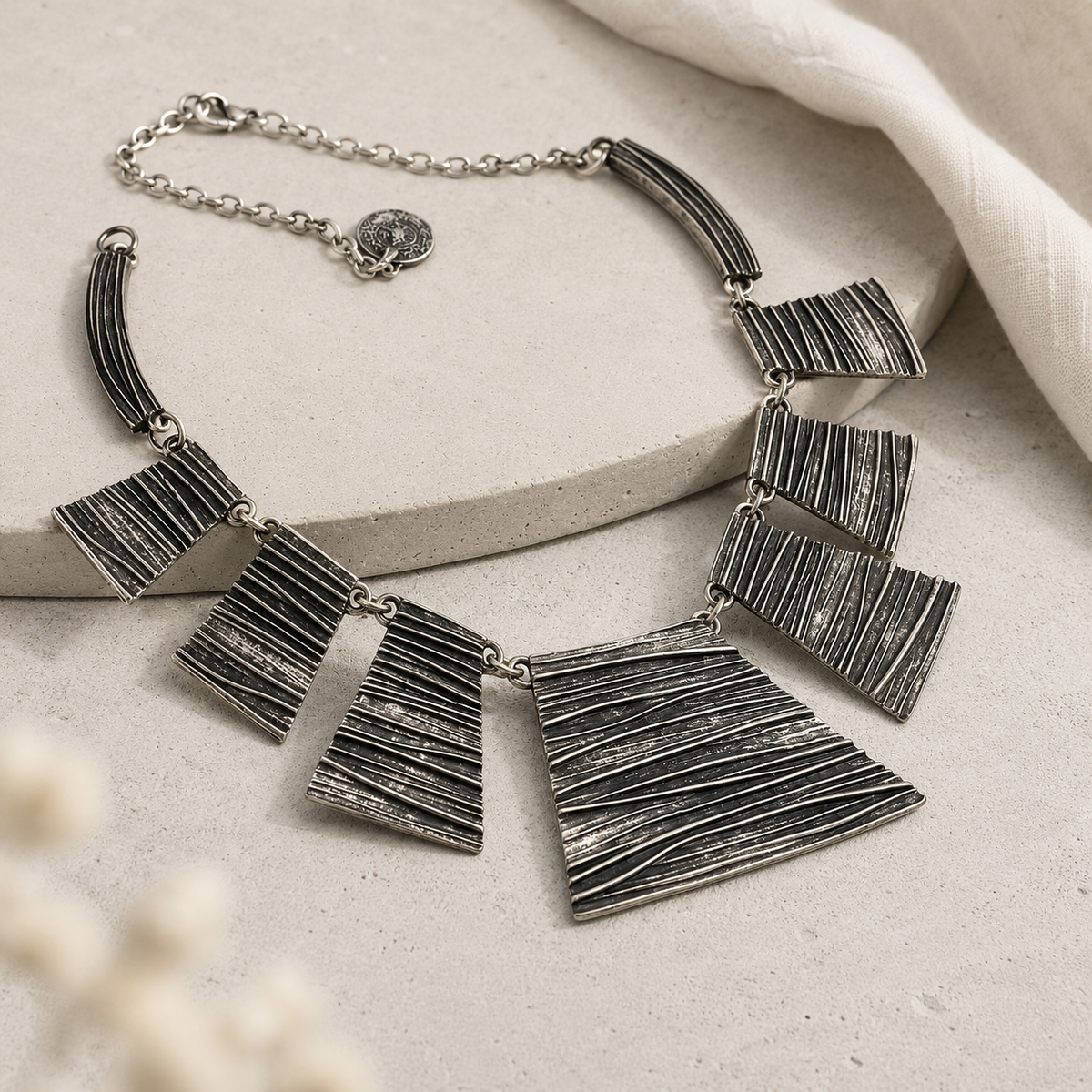 Angled view of a silver-tone necklace with textured panel details.