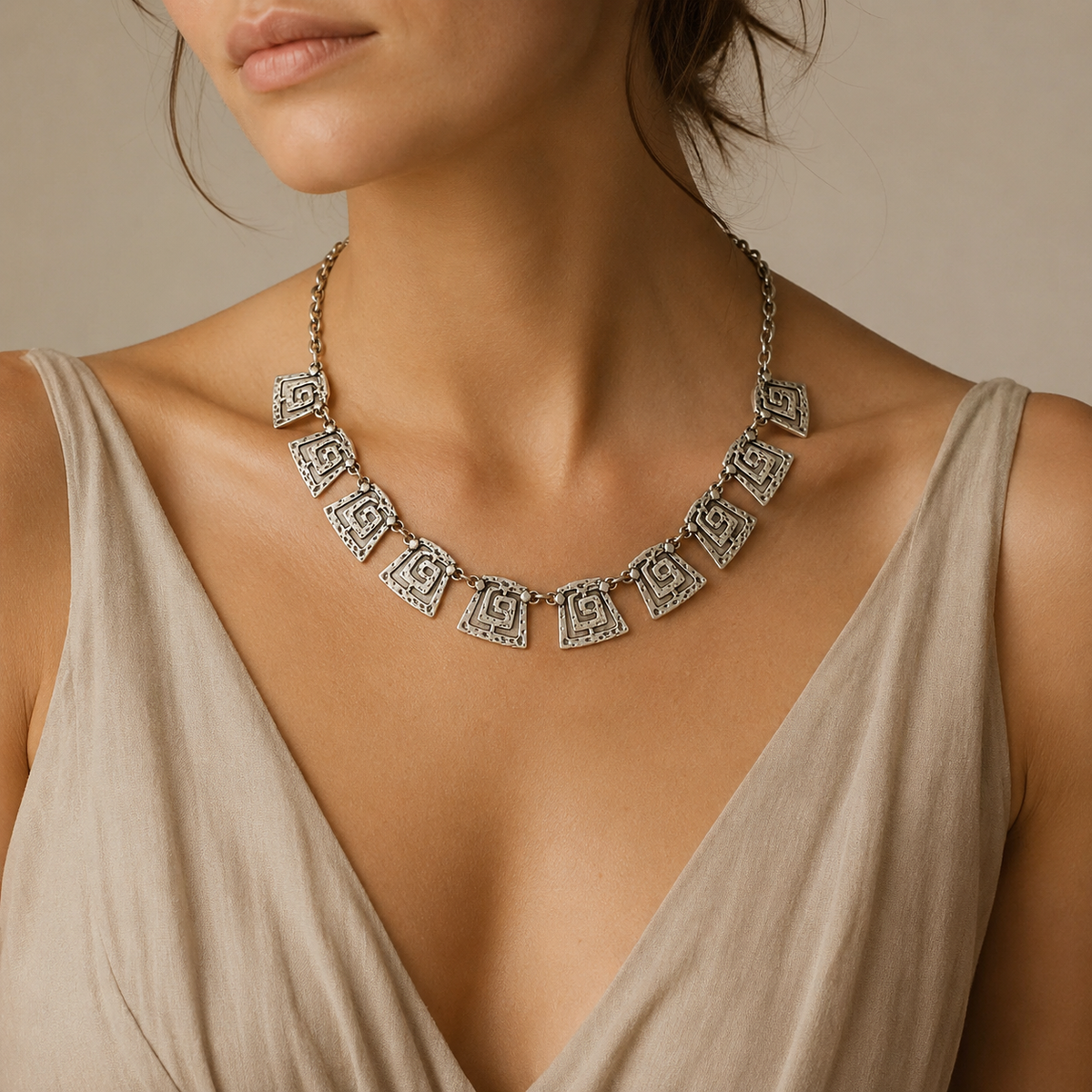 Silver-tone necklace featuring repeating spiral square links and a round clasp detail.