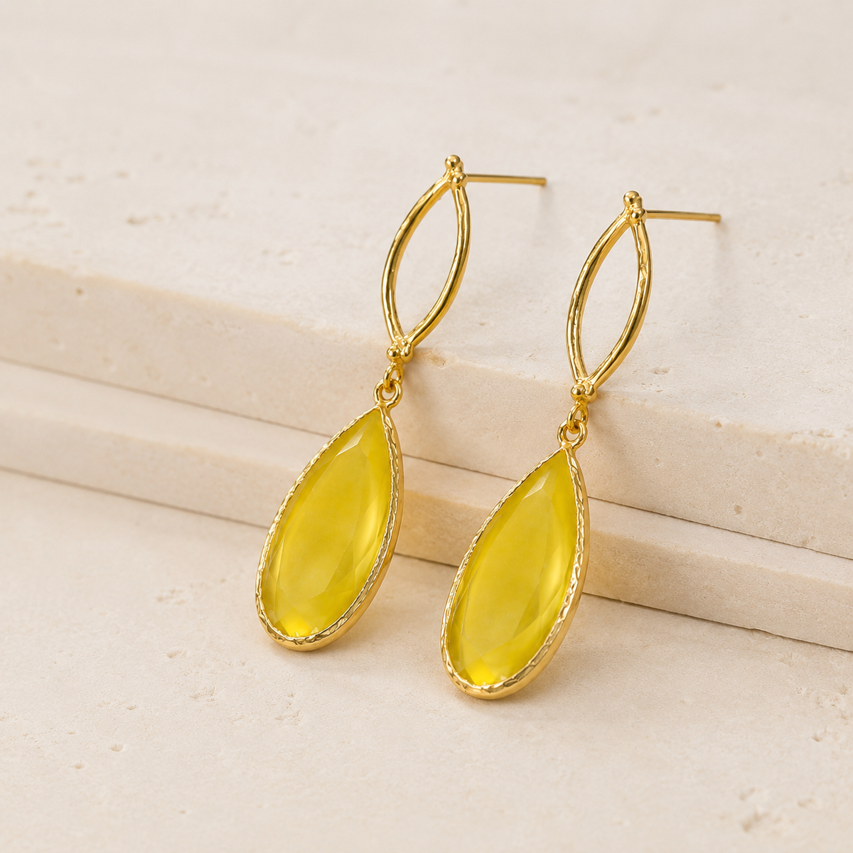Angled view of gold plated oval earrings with teardrop drops.