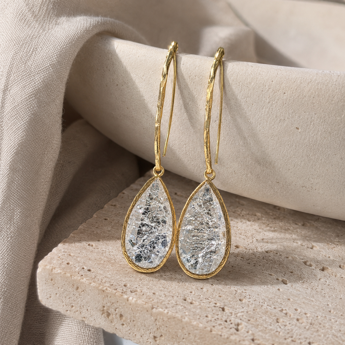 Angle view of gold-plated teardrop earrings with a cracked crystal finish.