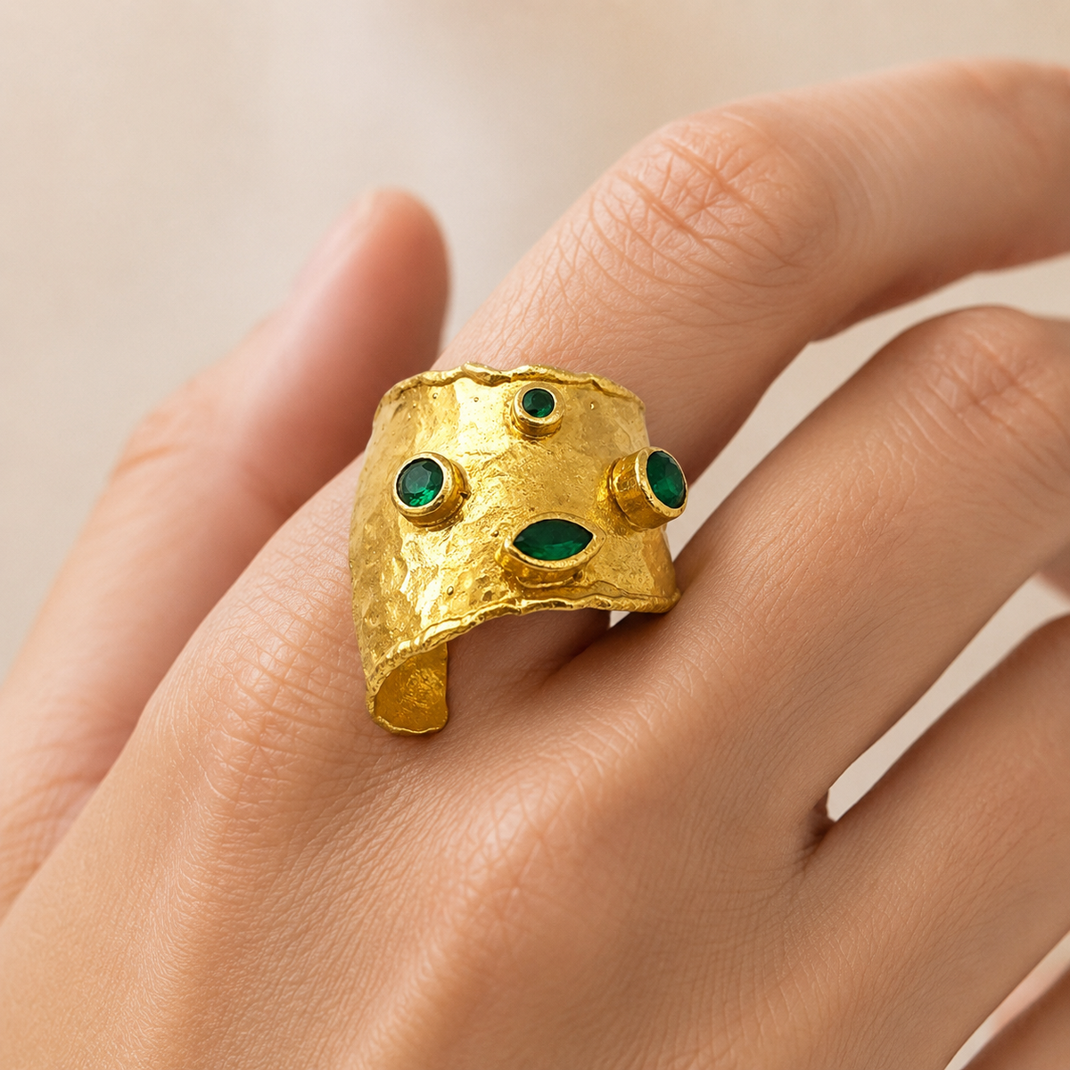 Gold-plated adjustable cuff ring with emerald green stones shown from a clean product angle.