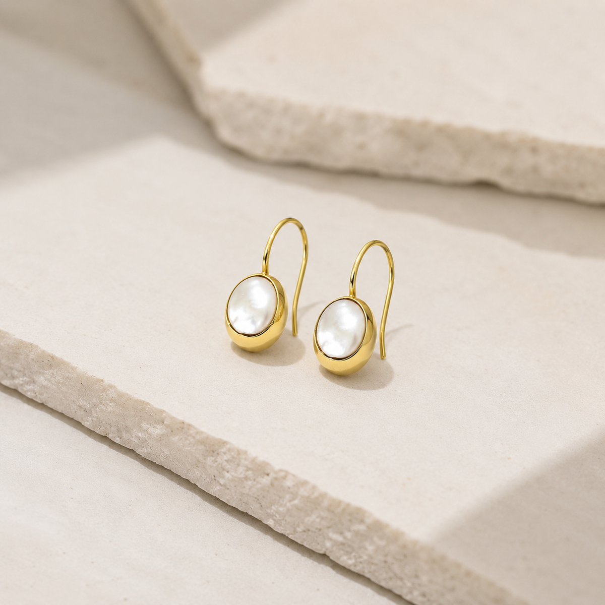 Angled view of gold-plated drop earrings with mother of pearl square accents.
