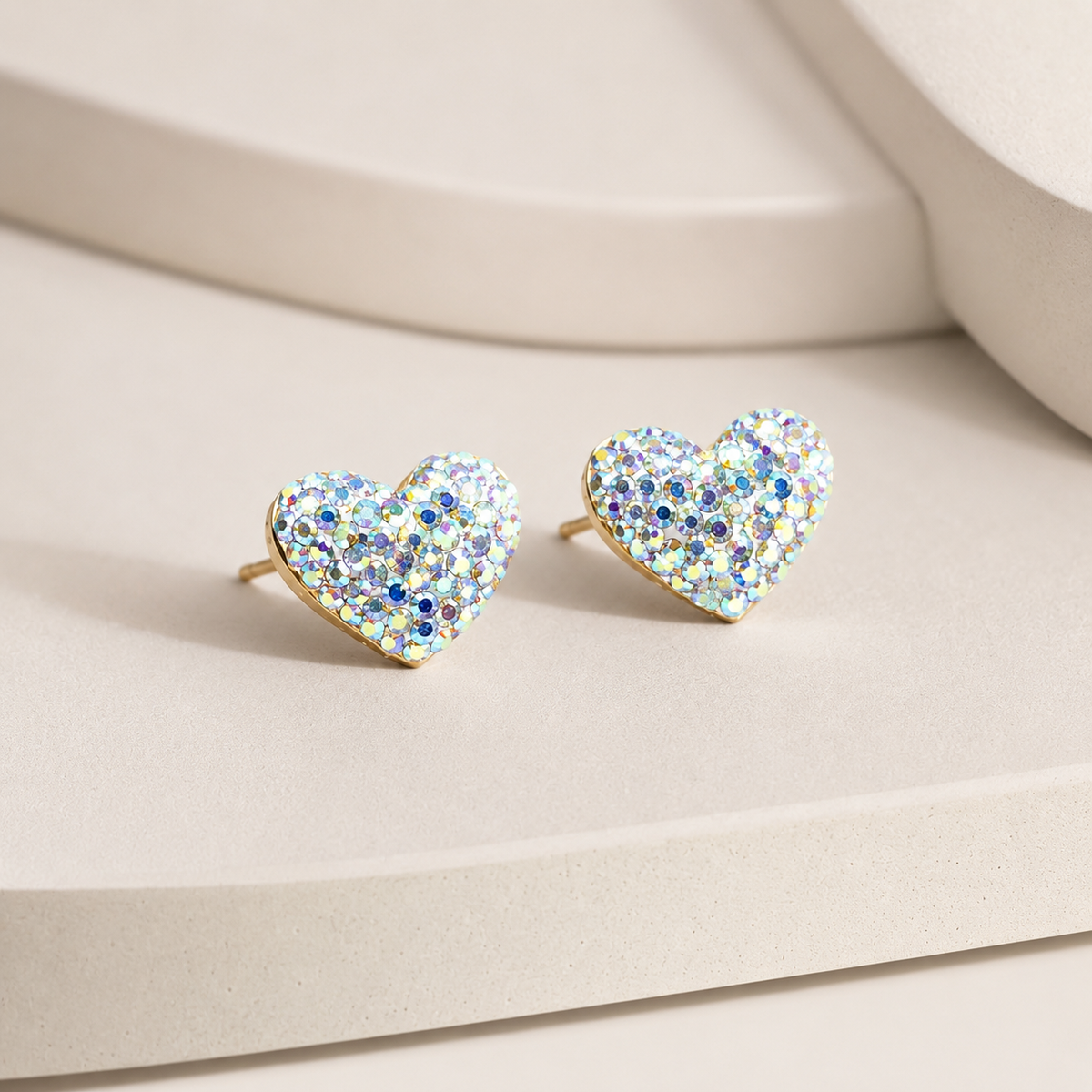 Angled view of heart-shaped stud earrings with a crystal-like sparkle and gold-tone base.