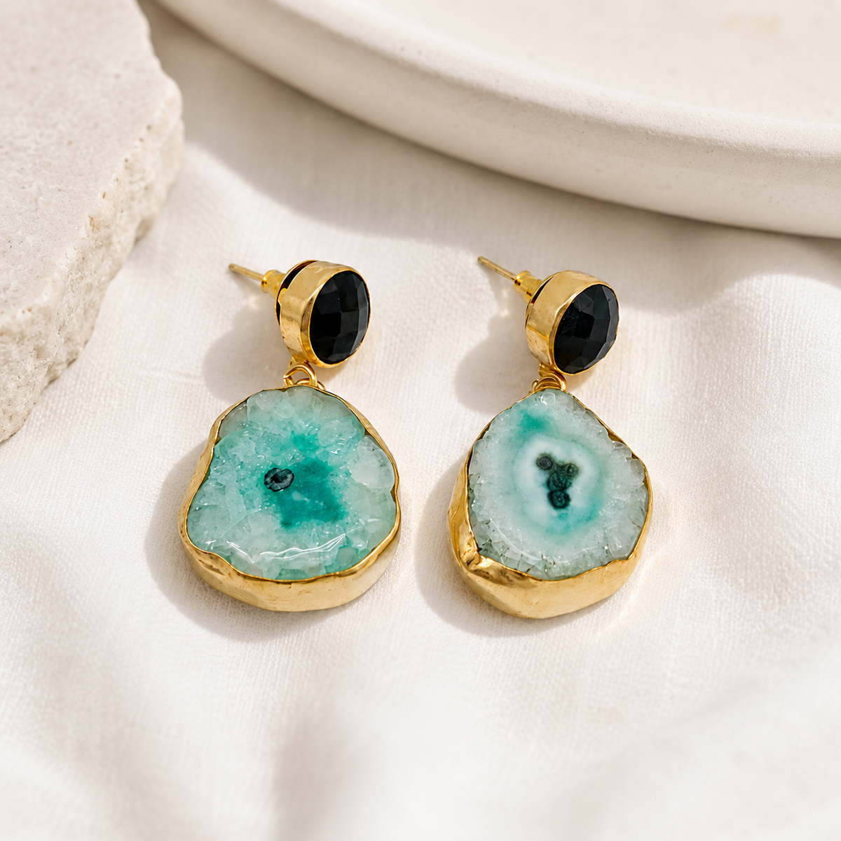 Gold-plated statement earrings with black stone tops and natural stone drops on a white background.
