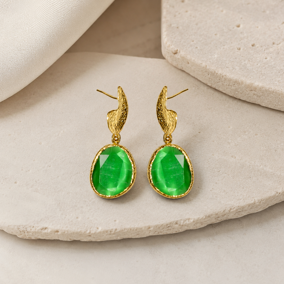 Long green stone drop earrings with a gold-plated finish on a white background.