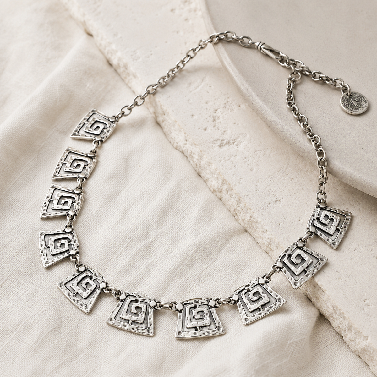 Angled view of a silver-tone spiral square link necklace with sculptural geometric shapes.