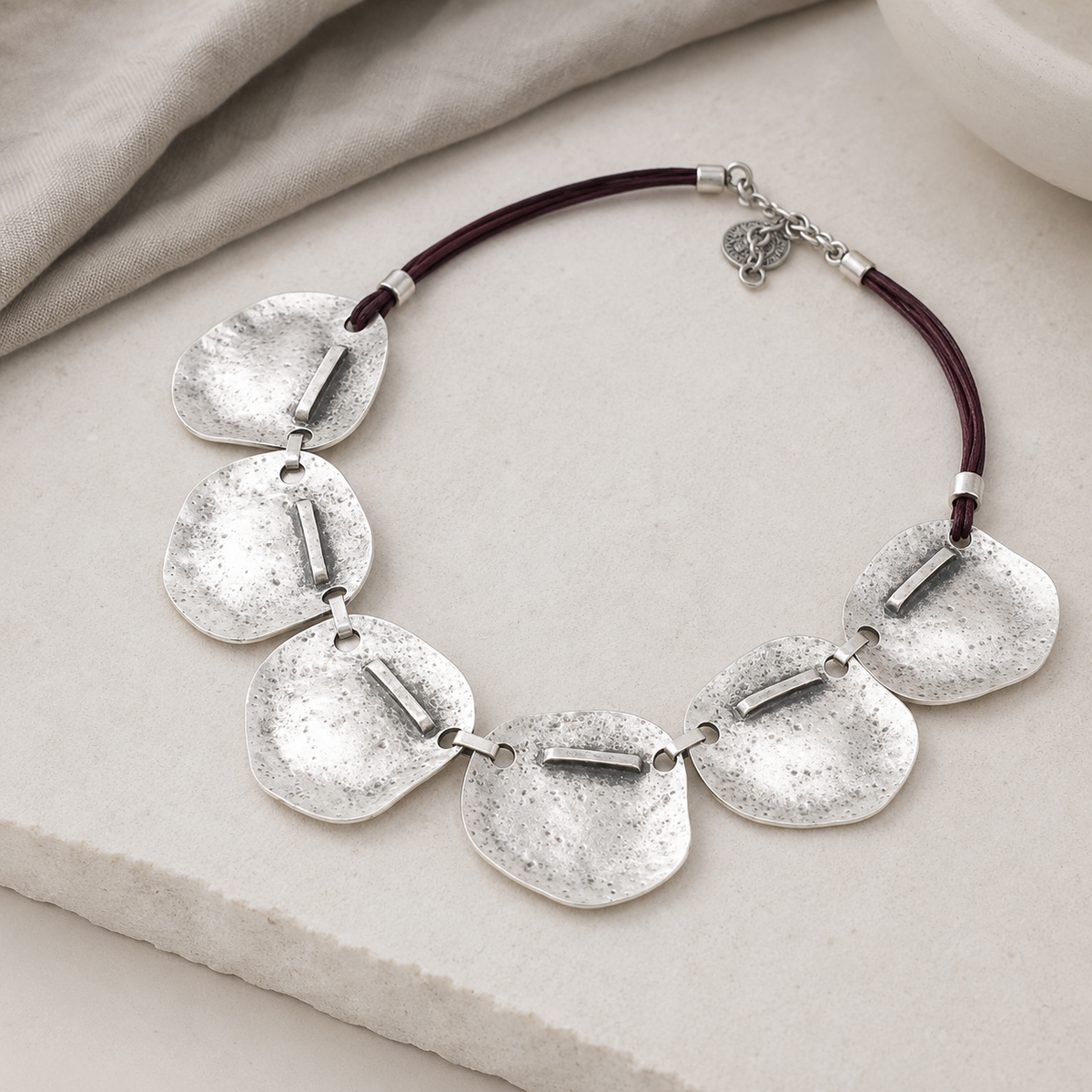Angled view of the hammered silver plate necklace with sculptural detail.