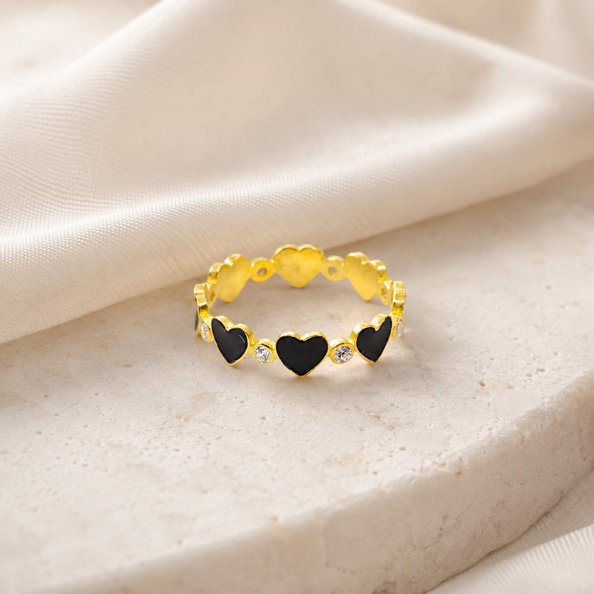 Gold-tone heart ring with black and clear accents on a white background.
