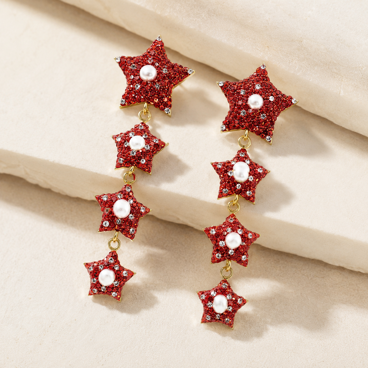 Side angle view of red star dangle earrings with pearl-like centers and gold-tone links.