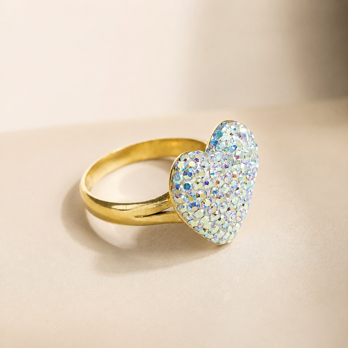 An angled view of a heart-shaped crystal ring with a polished gold-plated band.