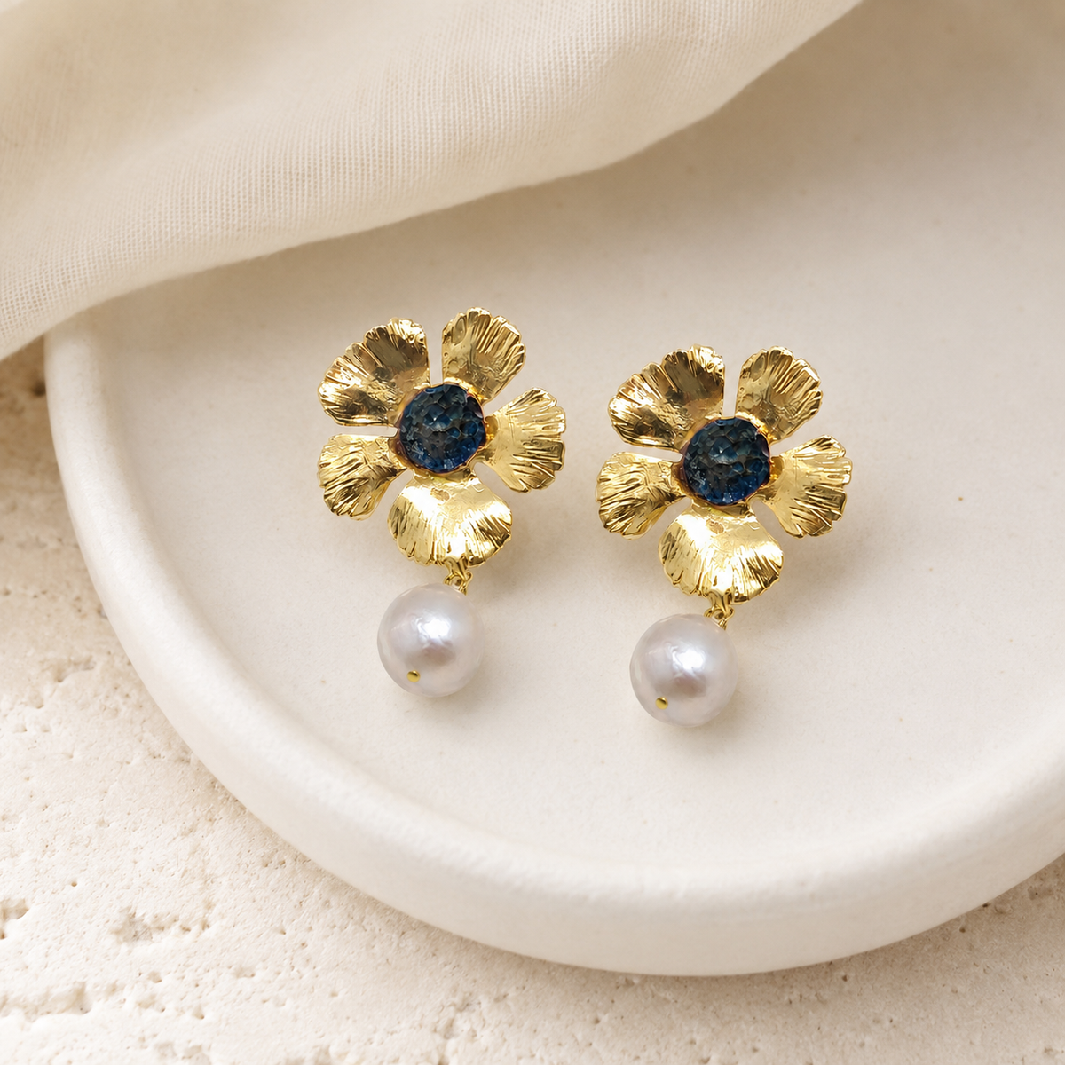 Gold flower drop earrings with a blue center and pearl drop on a white background.