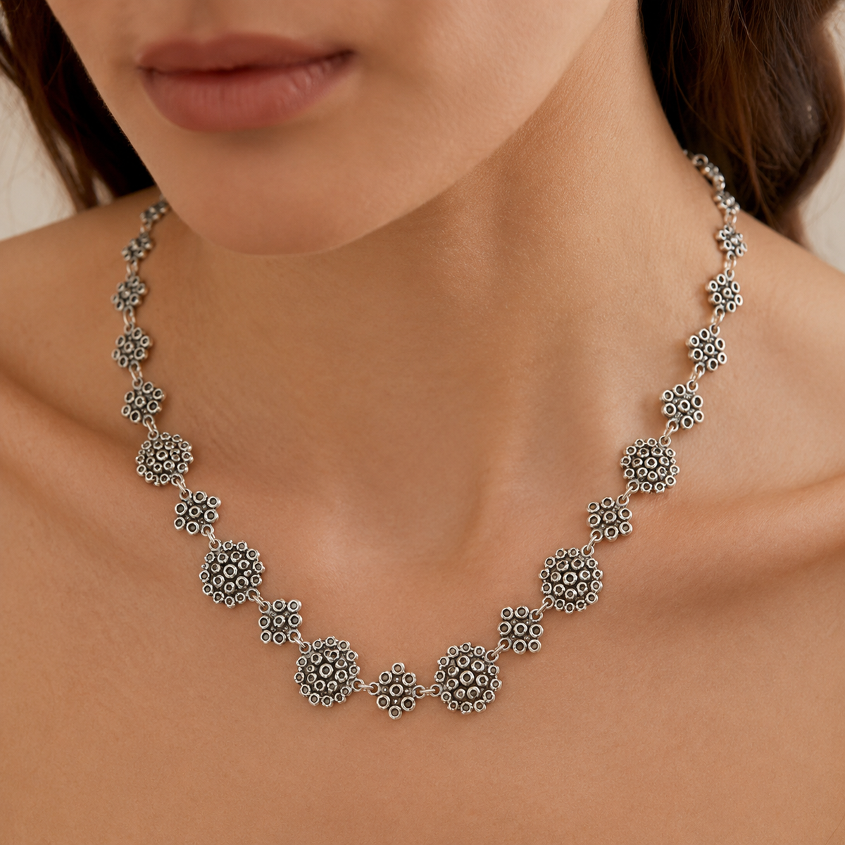 Silver-tone statement necklace with linked heart-inspired shapes shown from above.