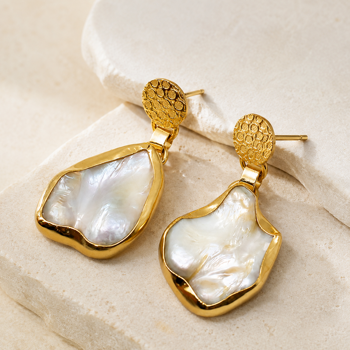 Angled view of gold-plated drop earrings with organic mother of pearl centers.